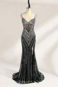 A mannequin numbered “6” displays a black tulle gown against a light backdrop. It features thin straps, a deep V - neckline, and a mermaid silhouette. The intricate silver bead patterns, sheer bodice with vertical accents, and high side slit add glamour, perfect for formal galas.1