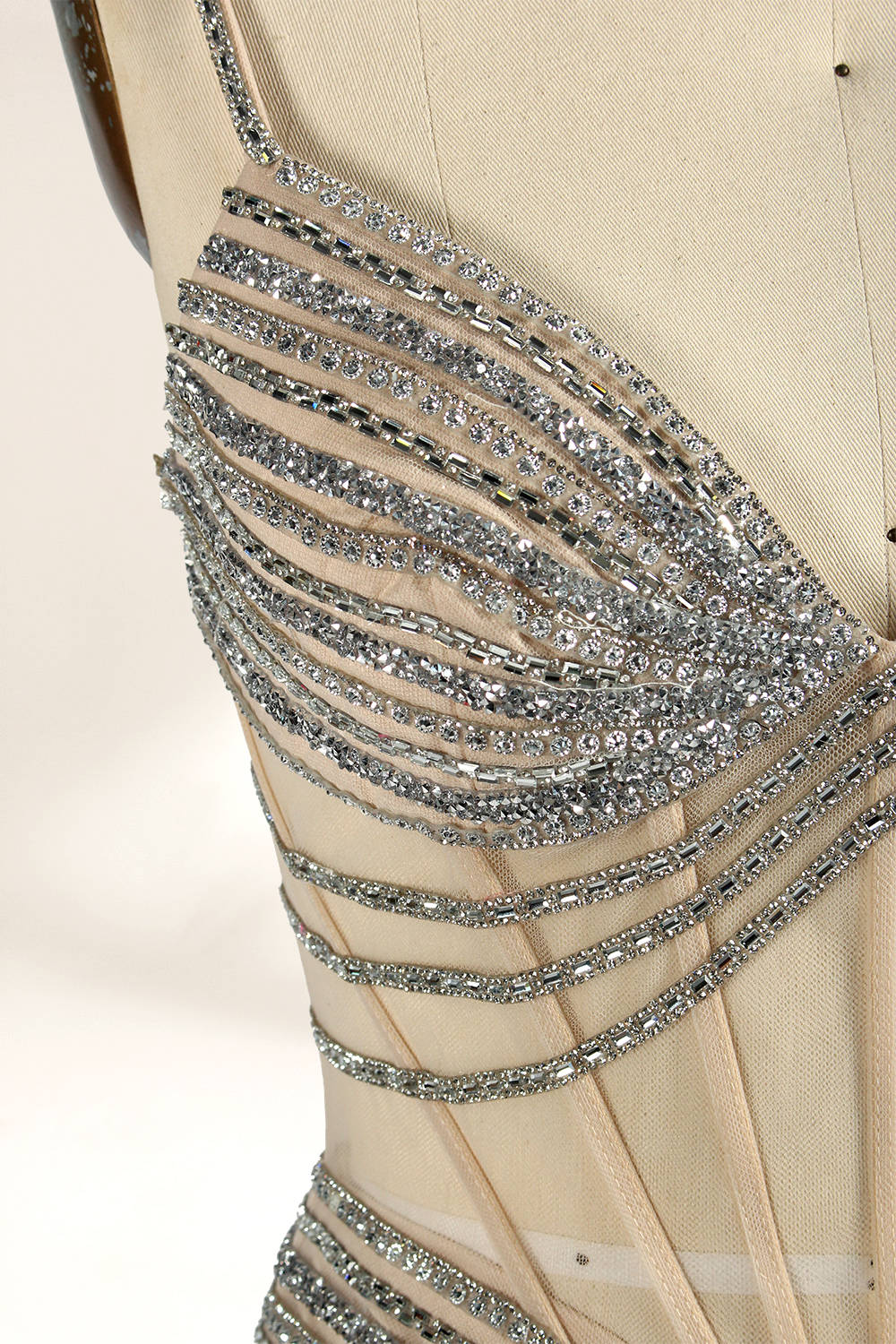 A mannequin numbered “6” displays a black tulle gown against a light backdrop. It features thin straps, a deep V - neckline, and a mermaid silhouette. The intricate silver bead patterns, sheer bodice with vertical accents, and high side slit add glamour, perfect for formal galas.7