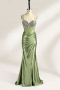 A mannequin presents a green satin gown with a bejeweled, sheer bodice against a light backdrop. It features thin straps, a sweetheart neckline, and a mermaid - shaped skirt. The sparkling embellishments and smooth fabric exude elegance, perfect for formal galas.1