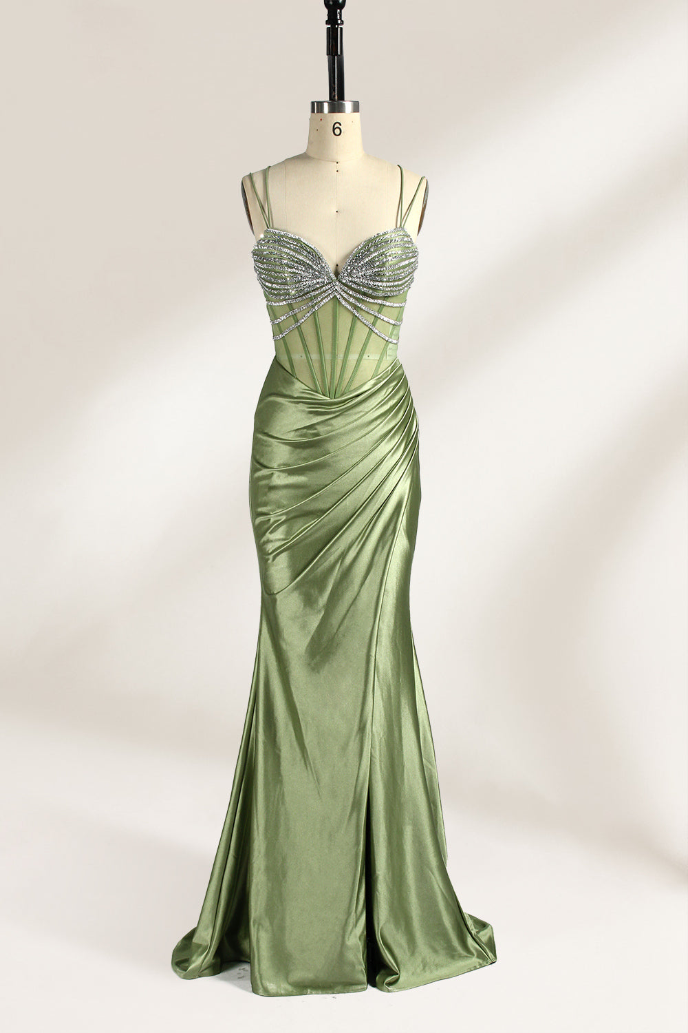 A mannequin presents a green satin gown with a bejeweled, sheer bodice against a light backdrop. It features thin straps, a sweetheart neckline, and a mermaid - shaped skirt. The sparkling embellishments and smooth fabric exude elegance, perfect for formal galas.1