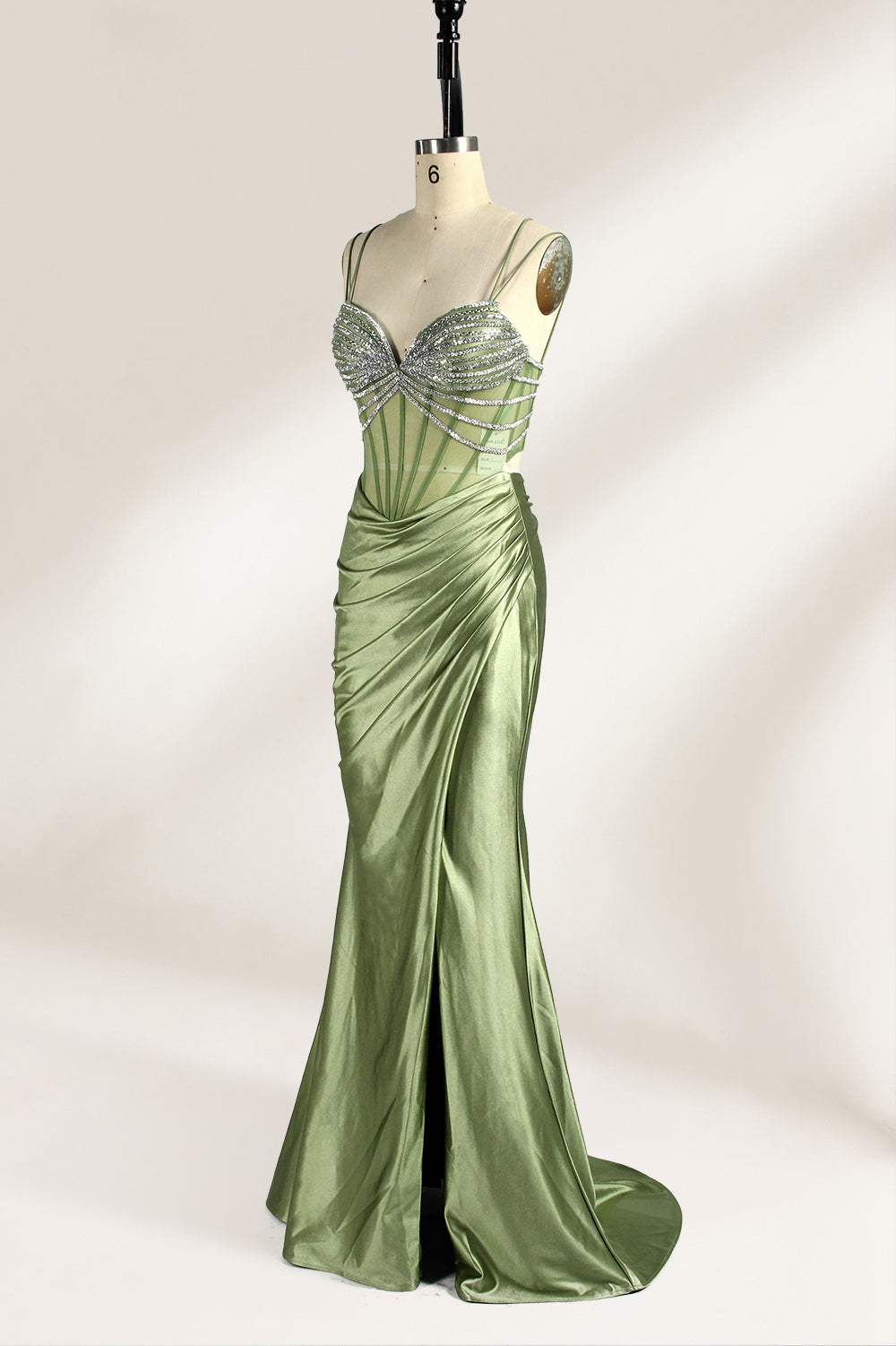 A mannequin presents a green satin gown with a bejeweled, sheer bodice against a light backdrop. It features thin straps, a sweetheart neckline, and a mermaid - shaped skirt. The sparkling embellishments and smooth fabric exude elegance, perfect for formal galas.3