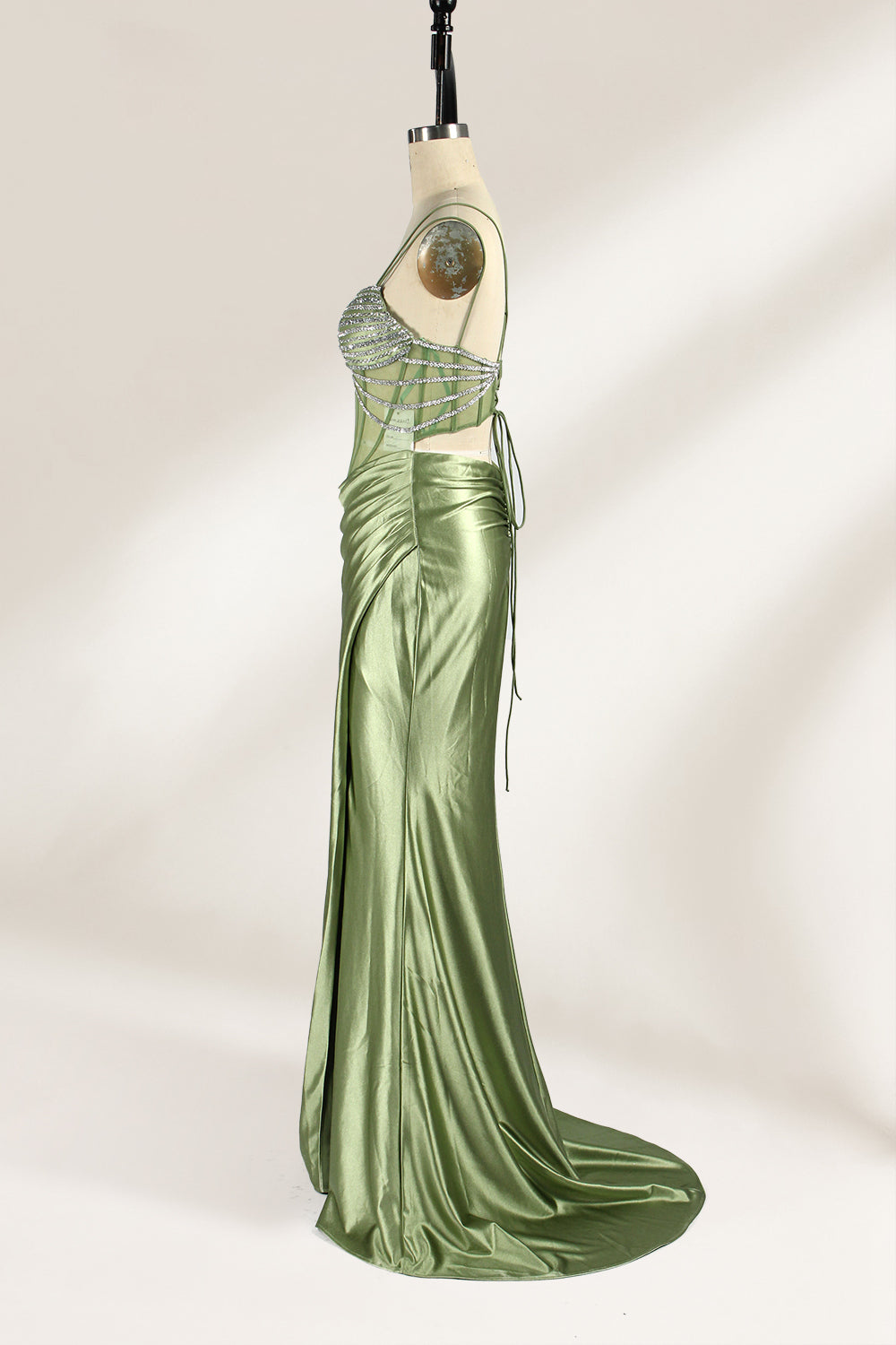 A mannequin presents a green satin gown with a bejeweled, sheer bodice against a light backdrop. It features thin straps, a sweetheart neckline, and a mermaid - shaped skirt. The sparkling embellishments and smooth fabric exude elegance, perfect for formal galas.4