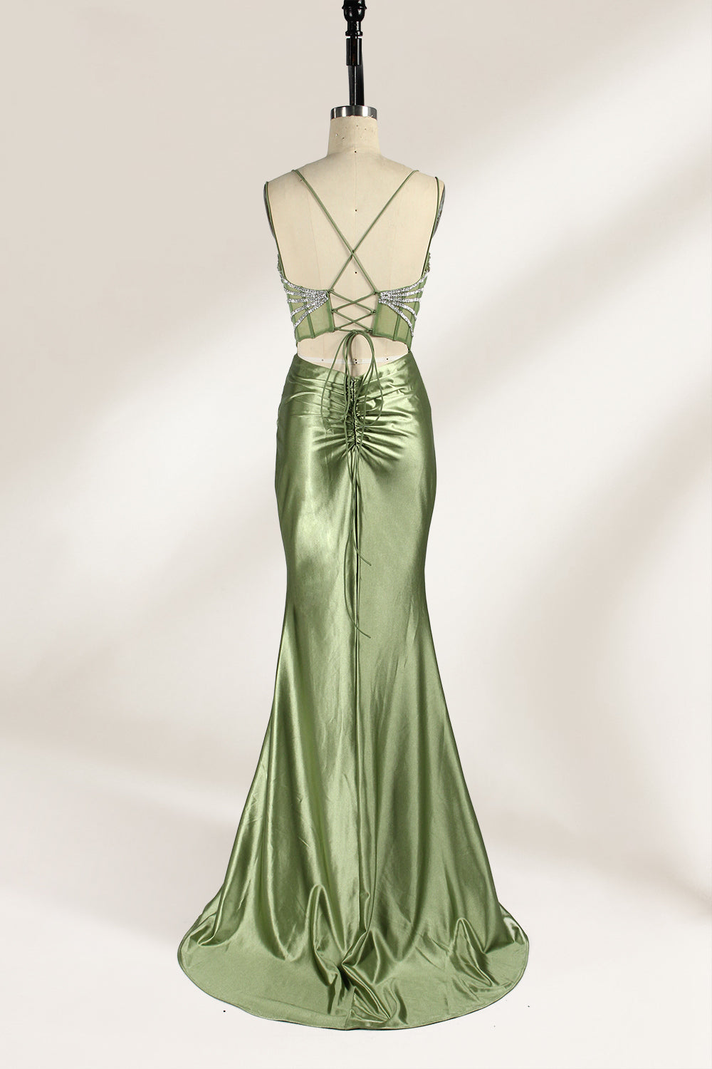 A mannequin presents a green satin gown with a bejeweled, sheer bodice against a light backdrop. It features thin straps, a sweetheart neckline, and a mermaid - shaped skirt. The sparkling embellishments and smooth fabric exude elegance, perfect for formal galas.2