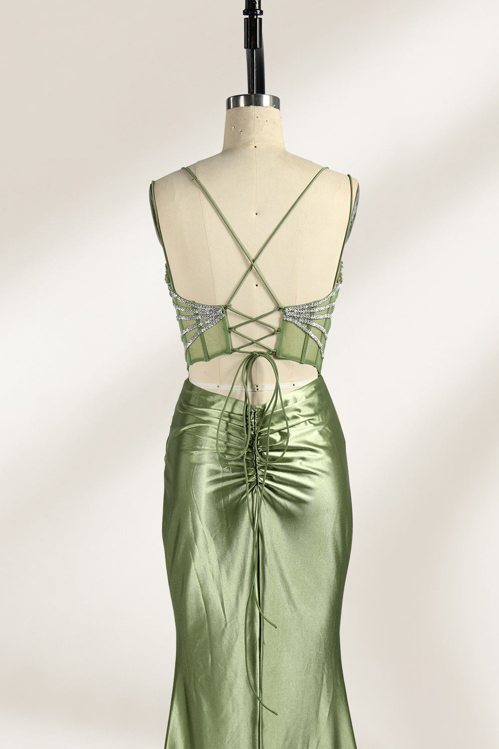 A mannequin presents a green satin gown with a bejeweled, sheer bodice against a light backdrop. It features thin straps, a sweetheart neckline, and a mermaid - shaped skirt. The sparkling embellishments and smooth fabric exude elegance, perfect for formal galas.5