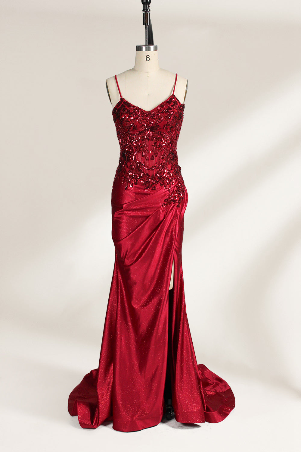 Photograph of a mannequin wearing a stunning, floor-length, navy blue satin evening gown. The gown features a deep V-back with thin straps and intricate sequin detailing along the back and neckline. The fitted bodice gradually flares into a flowing, elegant train. The mannequin stands against a plain, light beige backdrop, highlighting the gown's luxurious texture and shimmering finish. The gown exudes sophistication and glamour, ideal for formal events.1