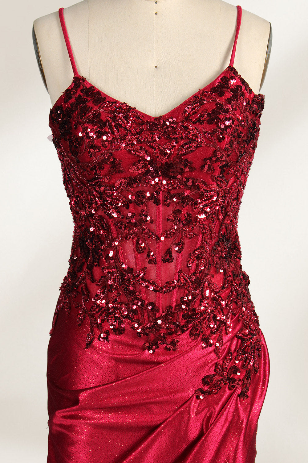 Photograph of a mannequin wearing a stunning, floor-length, navy blue satin evening gown. The gown features a deep V-back with thin straps and intricate sequin detailing along the back and neckline. The fitted bodice gradually flares into a flowing, elegant train. The mannequin stands against a plain, light beige backdrop, highlighting the gown's luxurious texture and shimmering finish. The gown exudes sophistication and glamour, ideal for formal events.3