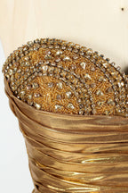A golden strapless evening gown is displayed on a mannequin. The bodice is adorned with intricate beadwork, and the skirt, made of a shiny metallic fabric, features a high side slit and a small train, creating a glamorous and elegant look, perfect for formal events.6