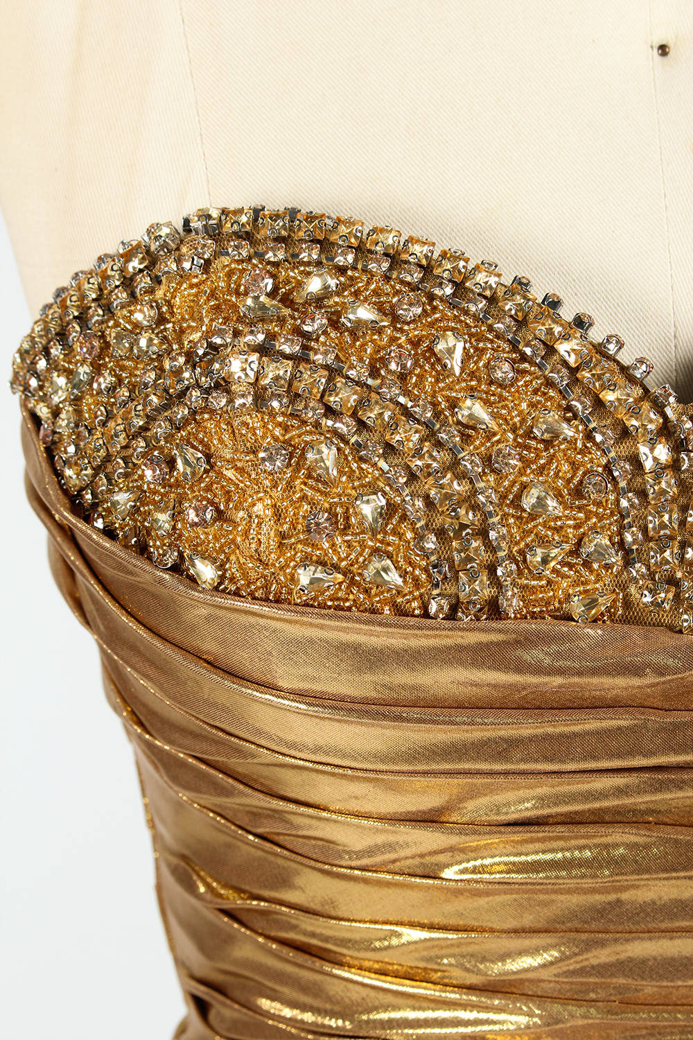A golden strapless evening gown is displayed on a mannequin. The bodice is adorned with intricate beadwork, and the skirt, made of a shiny metallic fabric, features a high side slit and a small train, creating a glamorous and elegant look, perfect for formal events.6