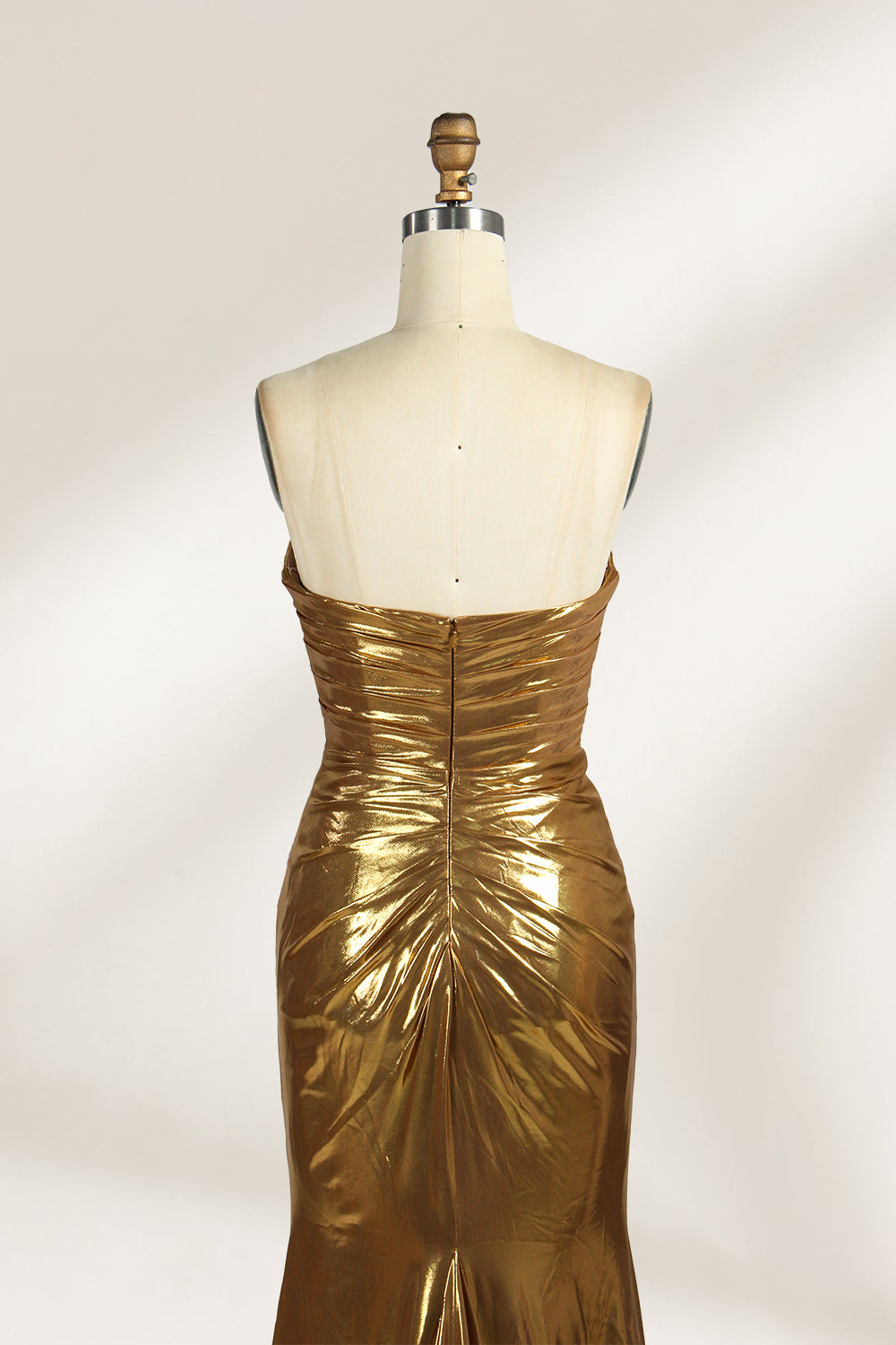 A golden strapless evening gown is displayed on a mannequin. The bodice is adorned with intricate beadwork, and the skirt, made of a shiny metallic fabric, features a high side slit and a small train, creating a glamorous and elegant look, perfect for formal events.5