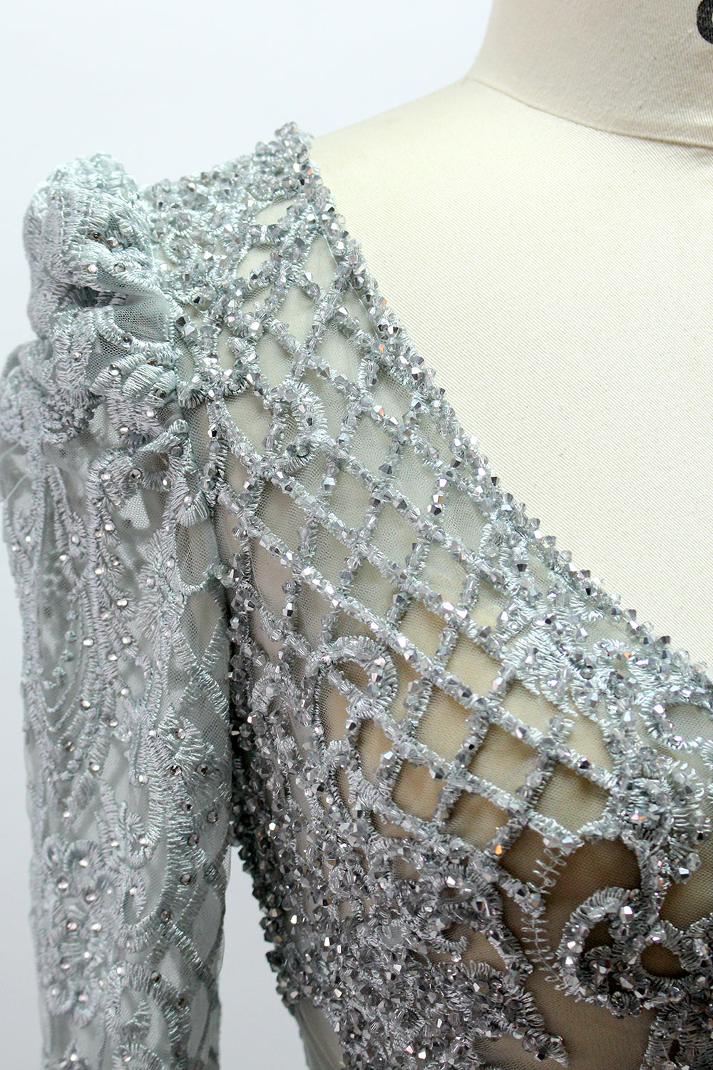 Displayed on a mannequin is a light - gray evening gown. It has a deep V - neckline, long sleeves, and intricate lace embroidery with a grid pattern. The elegant design gives off a luxurious and sophisticated vibe, ideal for formal occasions.9