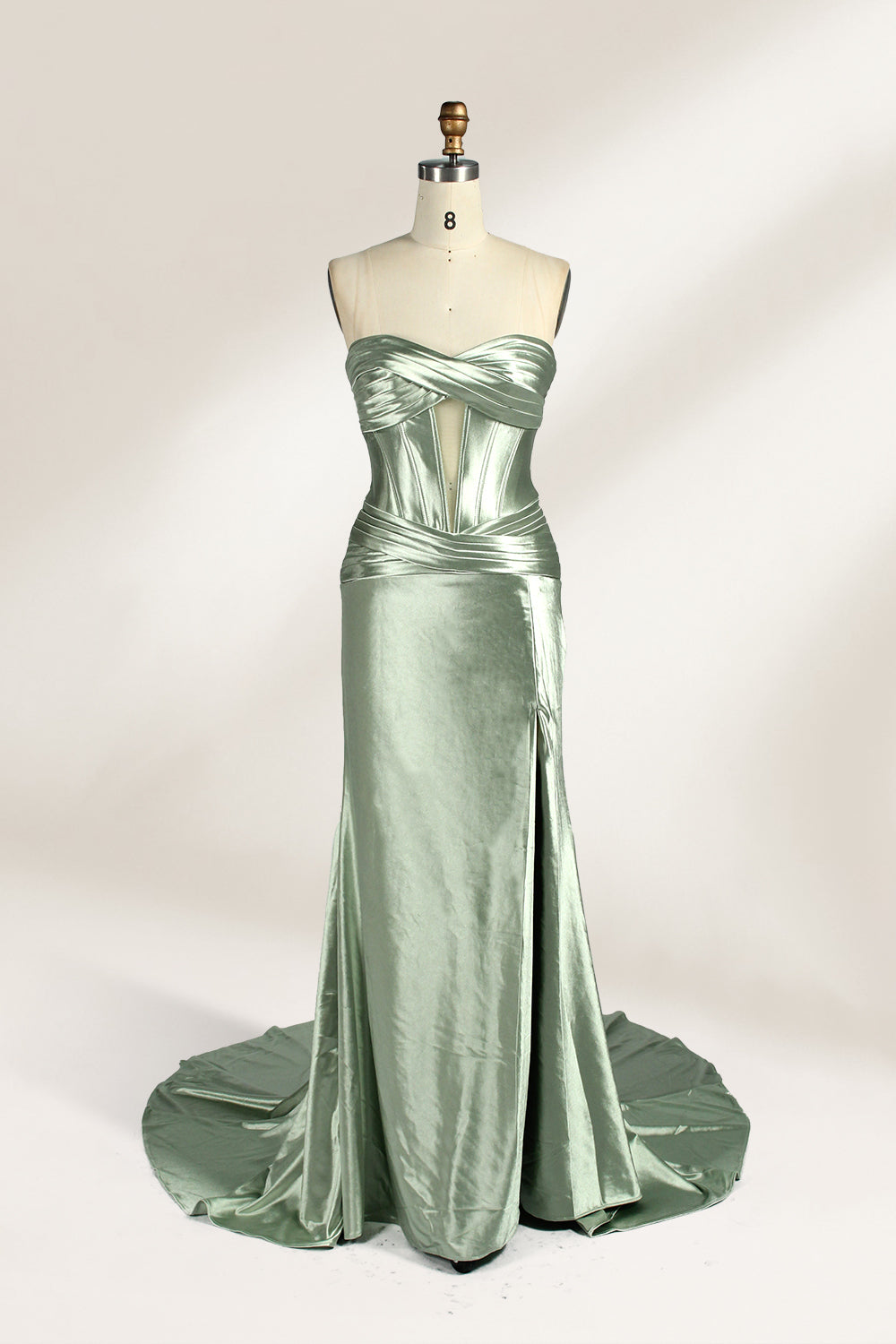 A mannequin showcases a strapless light - green satin gown against a soft, neutral backdrop. The dress features a twisted, criss - cross bodice with a subtle sheer panel and a mermaid silhouette, complete with a high side slit and a flowing train. The smooth, lustrous satin fabric and elegant design exude sophistication, perfect for formal galas or black - tie events.1