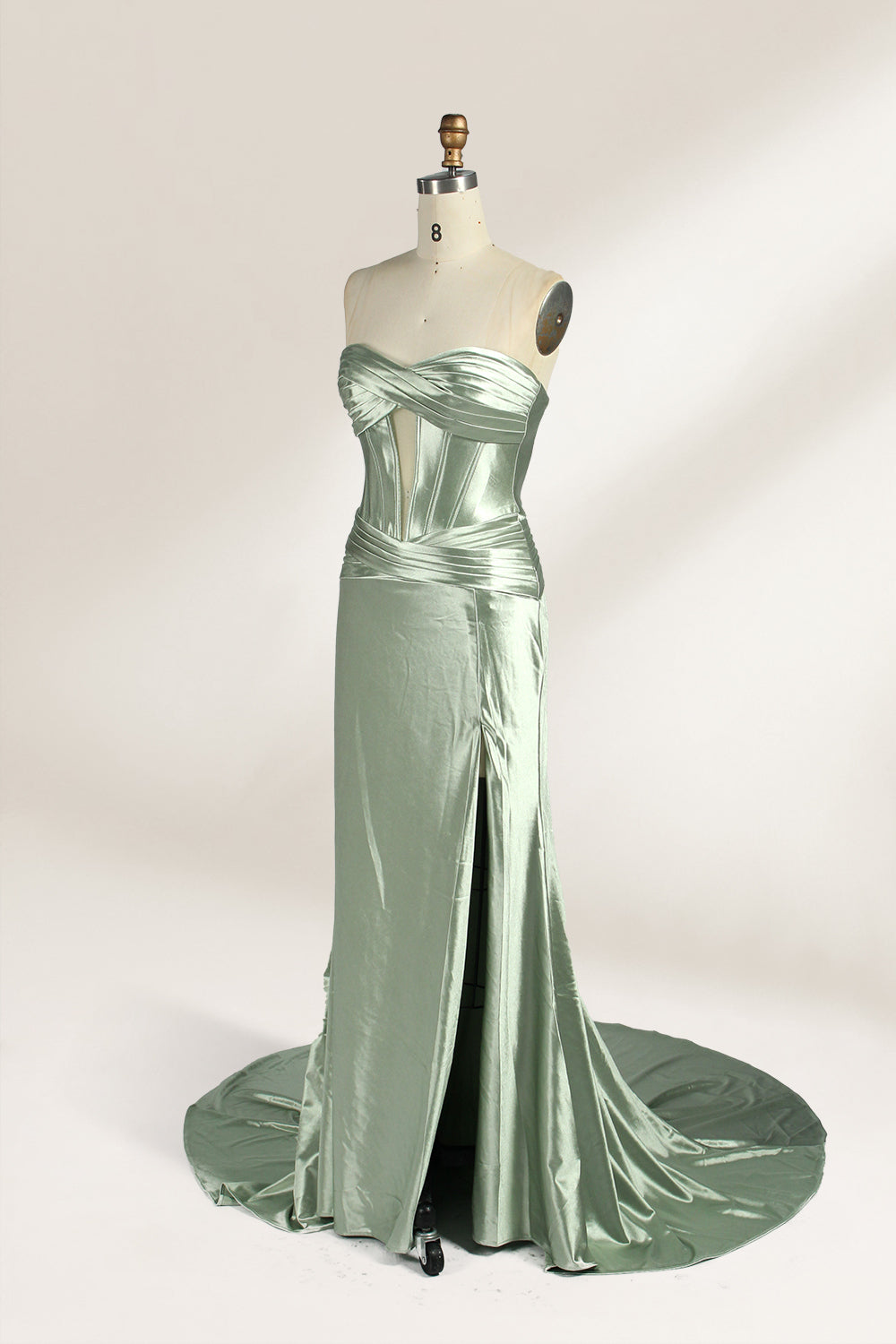 A mannequin showcases a strapless light - green satin gown against a soft, neutral backdrop. The dress features a twisted, criss - cross bodice with a subtle sheer panel and a mermaid silhouette, complete with a high side slit and a flowing train. The smooth, lustrous satin fabric and elegant design exude sophistication, perfect for formal galas or black - tie events.3