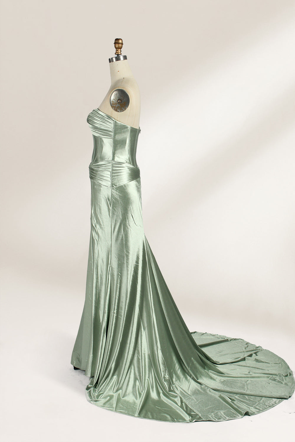 A mannequin showcases a strapless light - green satin gown against a soft, neutral backdrop. The dress features a twisted, criss - cross bodice with a subtle sheer panel and a mermaid silhouette, complete with a high side slit and a flowing train. The smooth, lustrous satin fabric and elegant design exude sophistication, perfect for formal galas or black - tie events.4