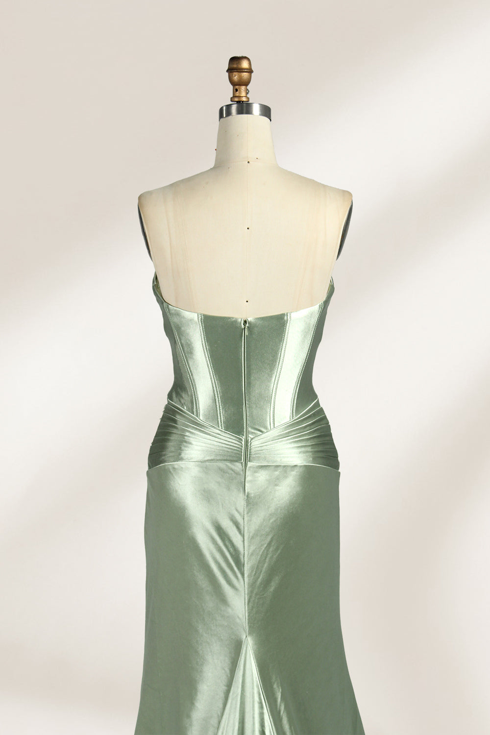 A mannequin showcases a strapless light - green satin gown against a soft, neutral backdrop. The dress features a twisted, criss - cross bodice with a subtle sheer panel and a mermaid silhouette, complete with a high side slit and a flowing train. The smooth, lustrous satin fabric and elegant design exude sophistication, perfect for formal galas or black - tie events.6