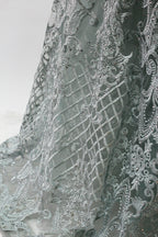 Displayed on a mannequin is a light - gray evening gown. It has a deep V - neckline, long sleeves, and intricate lace embroidery with a grid pattern. The elegant design gives off a luxurious and sophisticated vibe, ideal for formal occasions.10