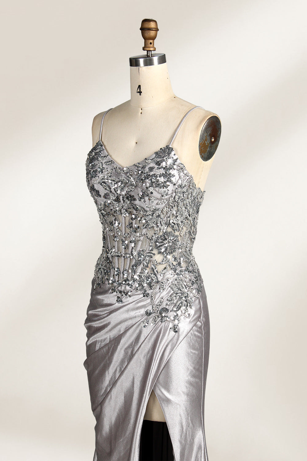 Photograph of a mannequin wearing a stunning, floor-length, navy blue satin evening gown. The gown features a deep V-back with thin straps and intricate sequin detailing along the back and neckline. The fitted bodice gradually flares into a flowing, elegant train. The mannequin stands against a plain, light beige backdrop, highlighting the gown's luxurious texture and shimmering finish. The gown exudes sophistication and glamour, ideal for formal events.6
