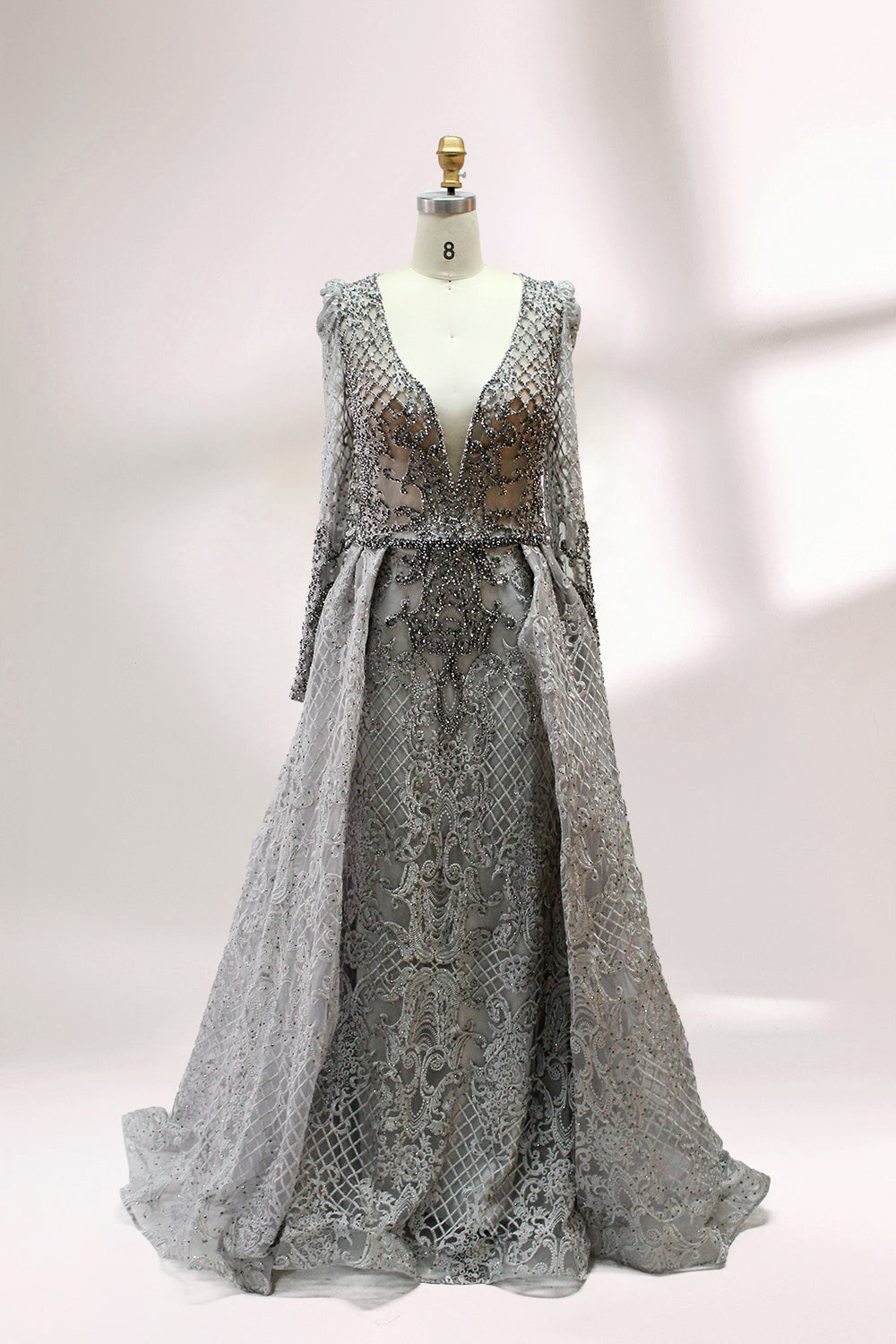 Displayed on a mannequin is a light - gray evening gown. It has a deep V - neckline, long sleeves, and intricate lace embroidery with a grid pattern. The elegant design gives off a luxurious and sophisticated vibe, ideal for formal occasions.3