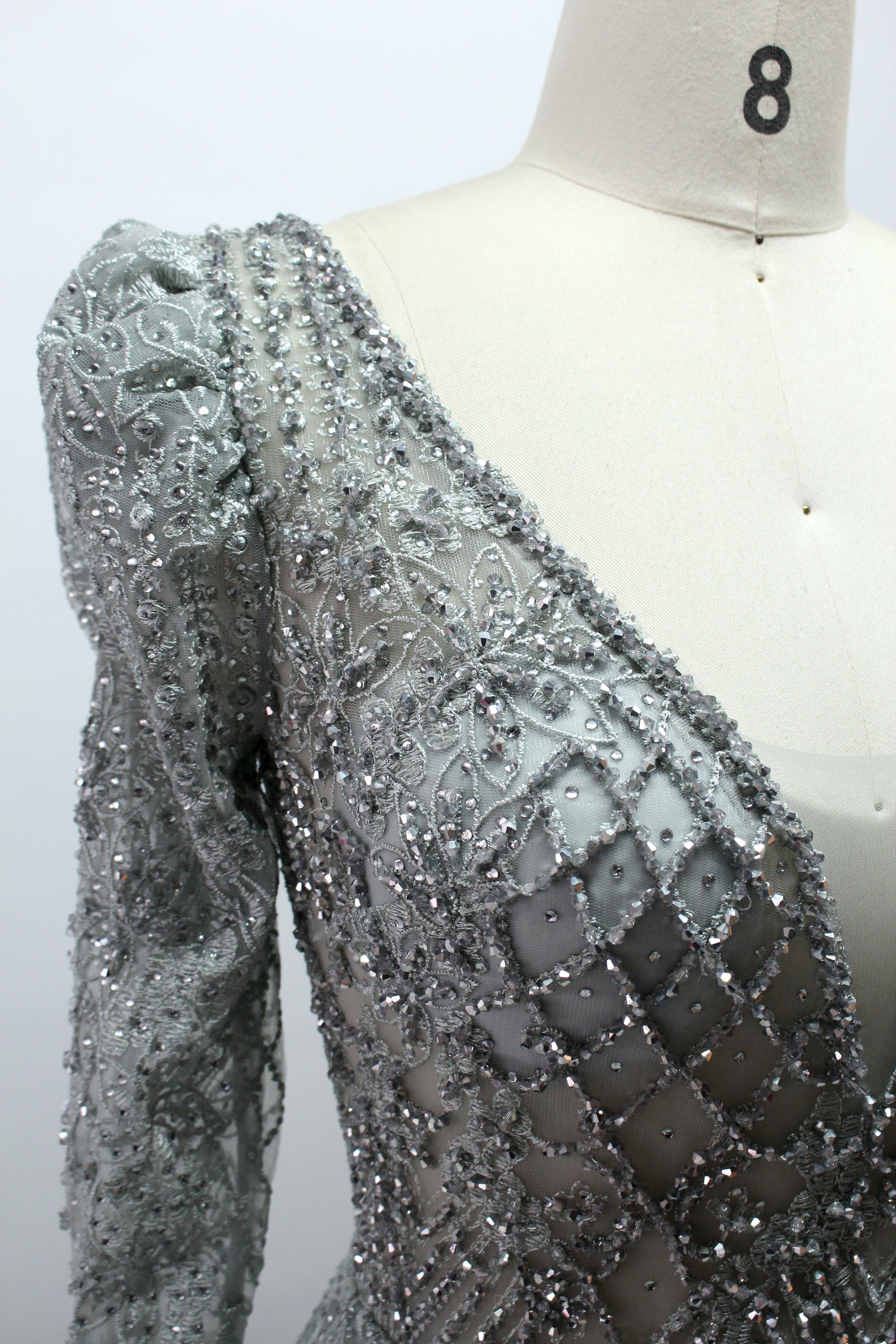 Illuminated softly, a mannequin showcases a light - gray evening gown. With a deep V - neckline, long puffed sleeves, and elaborate bead and lace embroidery, the gown exudes an air of luxury and sophistication, making it an excellent choice for formal galas and upscale events.10