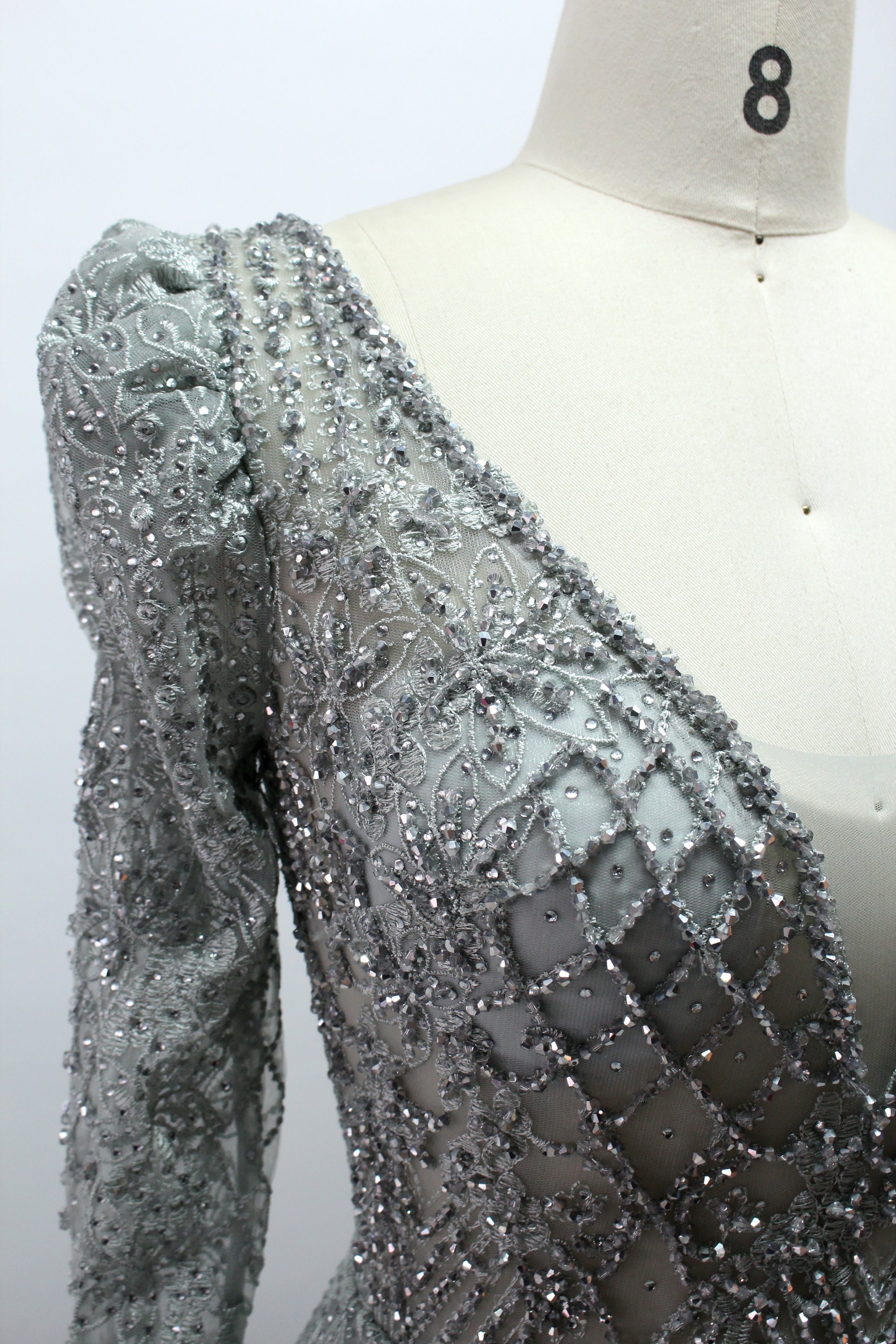Illuminated softly, a mannequin showcases a light - gray evening gown. With a deep V - neckline, long puffed sleeves, and elaborate bead and lace embroidery, the gown exudes an air of luxury and sophistication, making it an excellent choice for formal galas and upscale events.10