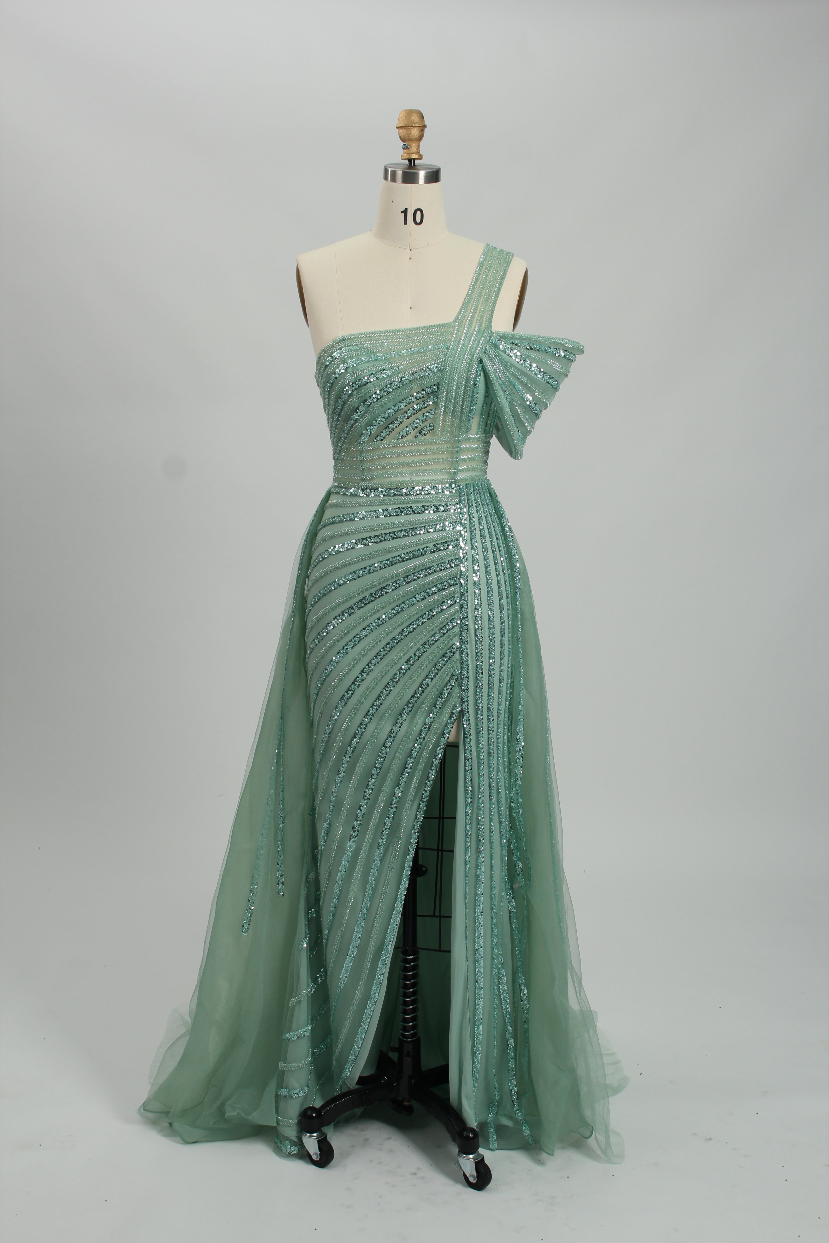 Against a light - hued backdrop, a woman dons a teal sequin gown with an one - shoulder design. It features a bow - detailed strap, a sheer waist panel, and a high side slit. The sparkling sequins and unique silhouette radiate glamour, perfect for formal dinners or galas.8
