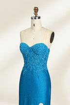 Photograph of a mannequin dressed in a strapless, floor-length, vibrant blue evening gown. The gown features intricate lace detailing across the bodice, with a fitted, corset-style silhouette. The skirt has a high slit on the right side, revealing black high heels underneath. The background is a plain, light beige, emphasizing the gown's shimmering texture and elegant design. The mannequin stands on a wooden base, labeled "4" on its neck.05