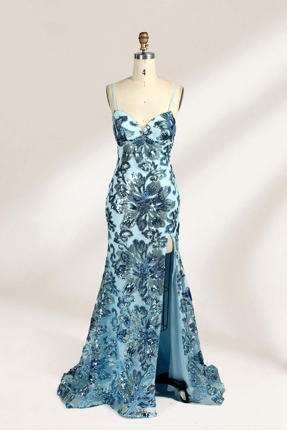Set against a light background, a mannequin presents a light - blue tulle gown adorned with intricate floral sequin patterns. It has thin spaghetti straps, a sweetheart neckline, and a mermaid - shaped skirt with a high side slit. The shimmering sequins and delicate design create a glamorous look, ideal for proms or formal evening events.1