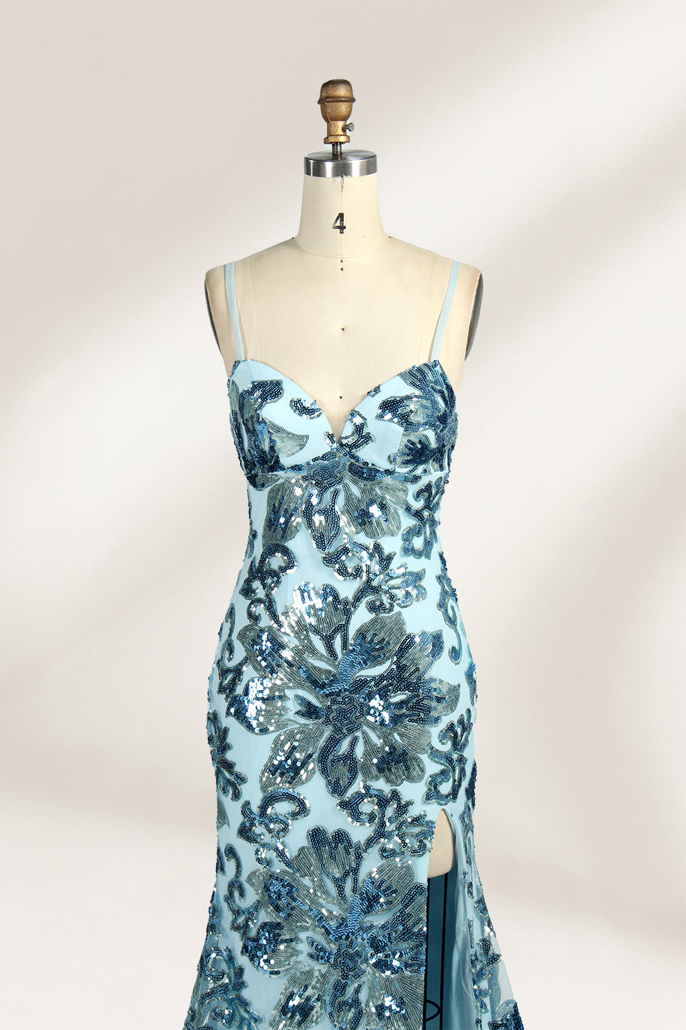 Set against a light background, a mannequin presents a light - blue tulle gown adorned with intricate floral sequin patterns. It has thin spaghetti straps, a sweetheart neckline, and a mermaid - shaped skirt with a high side slit. The shimmering sequins and delicate design create a glamorous look, ideal for proms or formal evening events.4