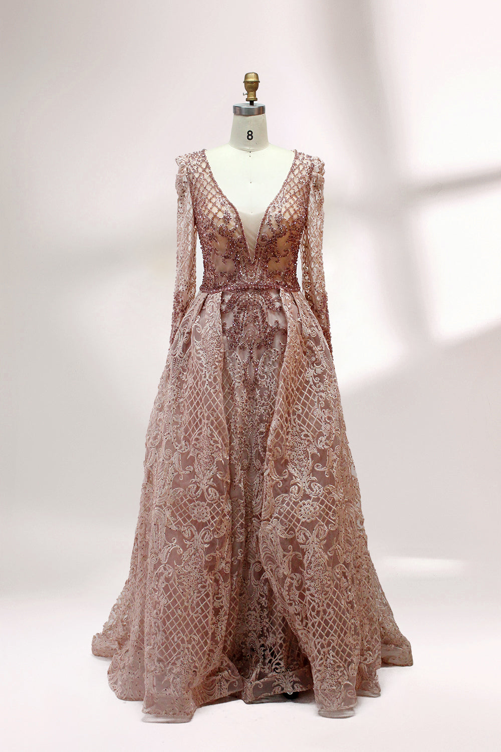 Displayed on a mannequin is a light - gray evening gown. It has a deep V - neckline, long sleeves, and intricate lace embroidery with a grid pattern. The elegant design gives off a luxurious and sophisticated vibe, ideal for formal occasions.4