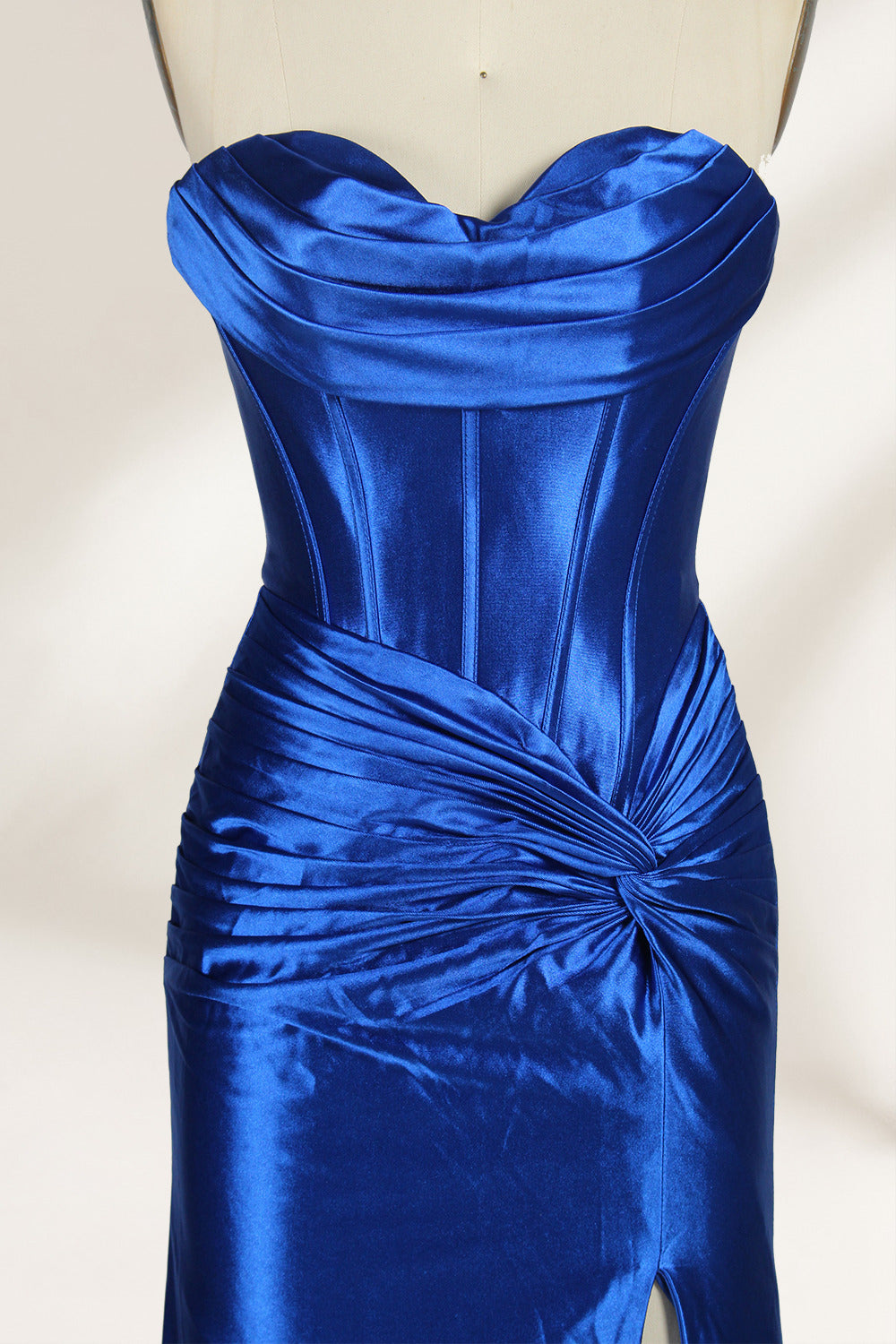 A mannequin showcases a strapless, blush - pink satin gown against a light backdrop. It features a ruched bodice with a draped neckline and a twisted detail at the waist, along with a mermaid silhouette and a side slit. The smooth satin fabric exudes elegance, perfect for formal events like galas.5