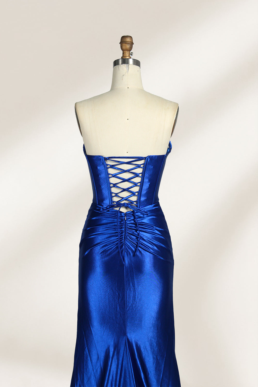 A mannequin showcases a strapless, blush - pink satin gown against a light backdrop. It features a ruched bodice with a draped neckline and a twisted detail at the waist, along with a mermaid silhouette and a side slit. The smooth satin fabric exudes elegance, perfect for formal events like galas.4