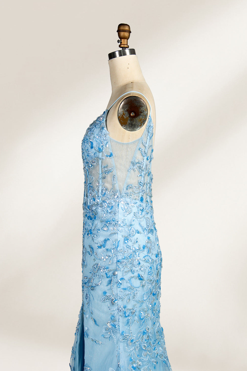A mannequin showcases a light - blue tulle gown. It has thin straps, a V - neck, floral embroidery, and a high side slit. The intricate design, with sheer bodice details, suits formal events like galas or proms, radiating elegance and charm.5
