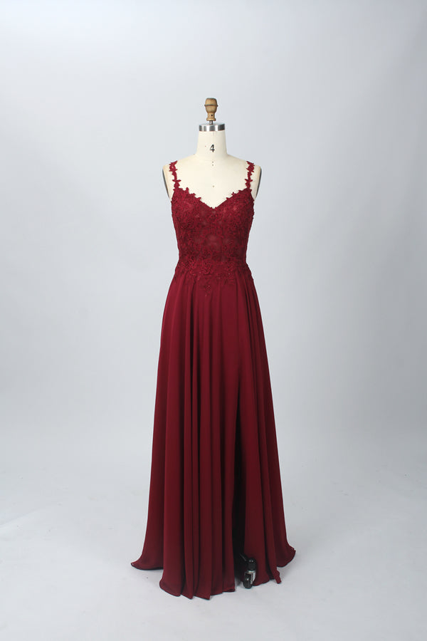 Photograph of a blue, floor-length, sleeveless gown with intricate lace detailing on the bodice and a subtle thigh-high slit, displayed on a mannequin. The gown has a fitted top and a flowing, soft fabric skirt. The background is plain beige.07