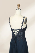 Photograph of a blue, floor-length, sleeveless gown with intricate lace detailing on the bodice and a subtle thigh-high slit, displayed on a mannequin. The gown has a fitted top and a flowing, soft fabric skirt. The background is plain beige.04