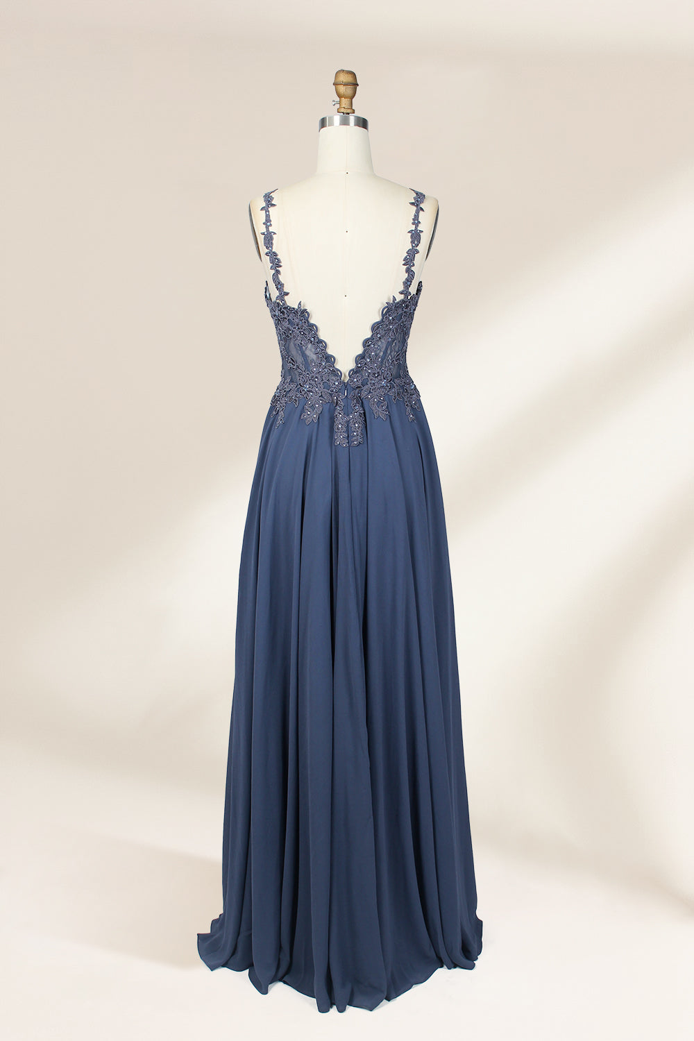 Photograph of a blue, floor-length, sleeveless gown with intricate lace detailing on the bodice and a subtle thigh-high slit, displayed on a mannequin. The gown has a fitted top and a flowing, soft fabric skirt. The background is plain beige.02