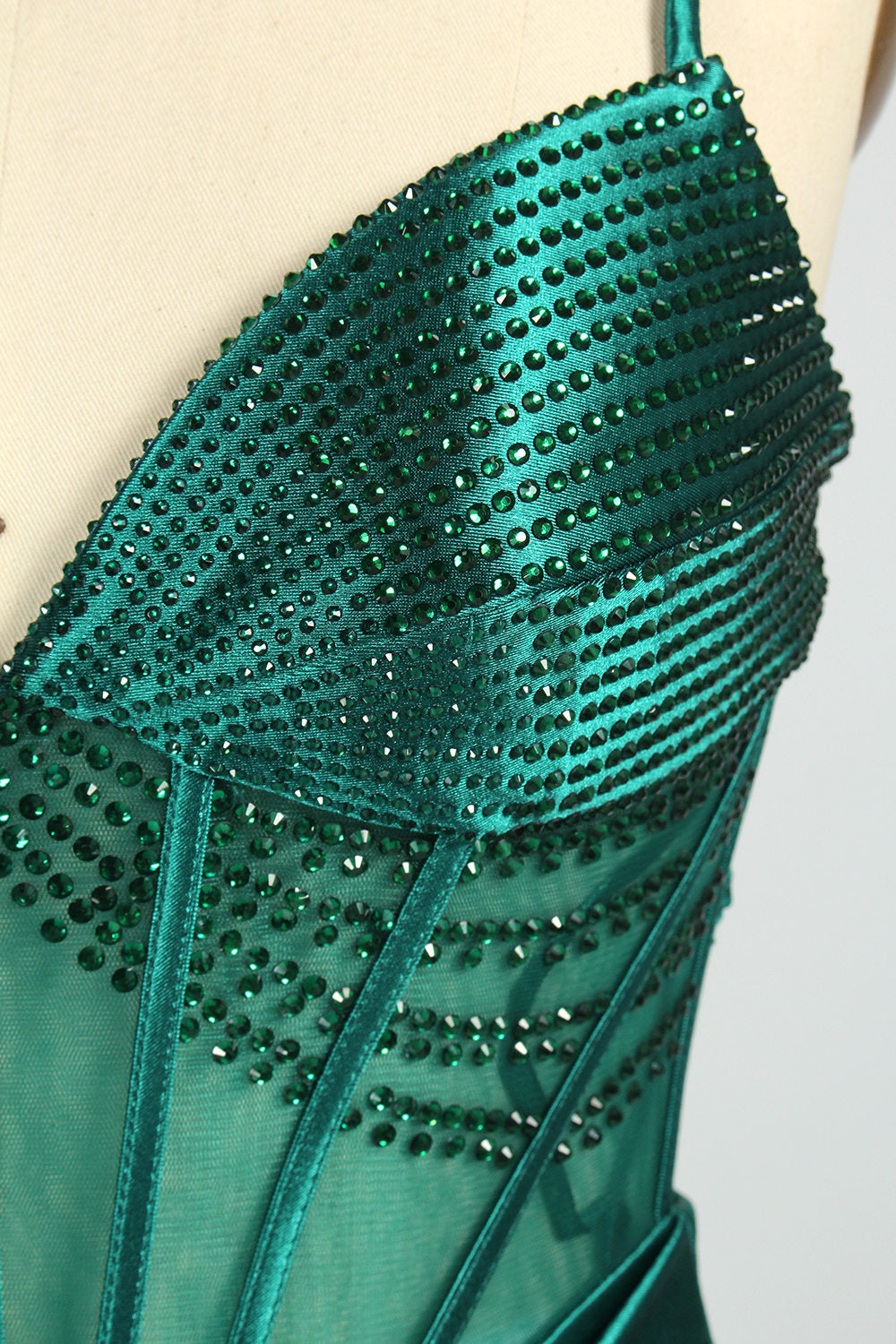 A mannequin displays a green satin gown against a light backdrop. It has thin straps, a sweetheart neckline, and a sheer bodice with beading. The mermaid skirt, featuring a high side slit, combines elegance and allure, perfect for formal galas.7