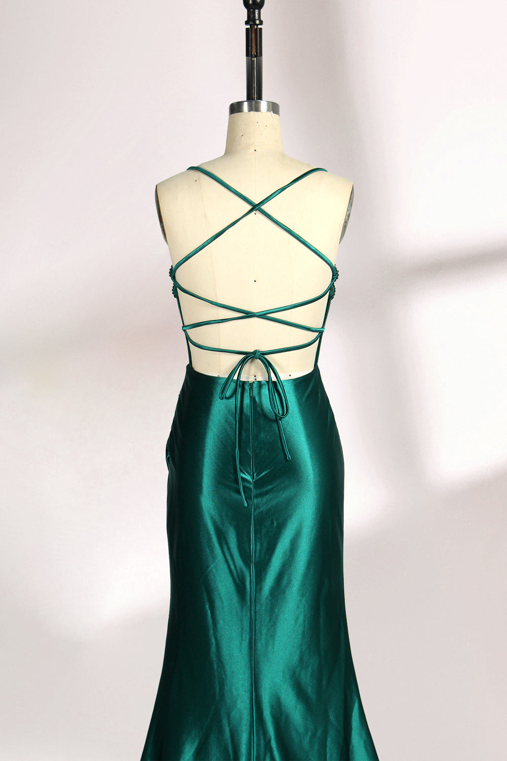 A mannequin displays a green satin gown against a light backdrop. It has thin straps, a sweetheart neckline, and a sheer bodice with beading. The mermaid skirt, featuring a high side slit, combines elegance and allure, perfect for formal galas.6 