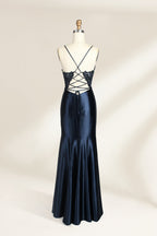 Photograph of a mannequin showcasing a floor-length, navy blue satin evening gown with intricate black sequin embroidery on the bodice and straps. The gown features a deep V-neckline, spaghetti straps, and a high slit on the right side. The background is a plain, light beige wall, enhancing the dress's elegant, sophisticated design.02