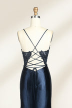 Photograph of a mannequin showcasing a floor-length, navy blue satin evening gown with intricate black sequin embroidery on the bodice and straps. The gown features a deep V-neckline, spaghetti straps, and a high slit on the right side. The background is a plain, light beige wall, enhancing the dress's elegant, sophisticated design.05