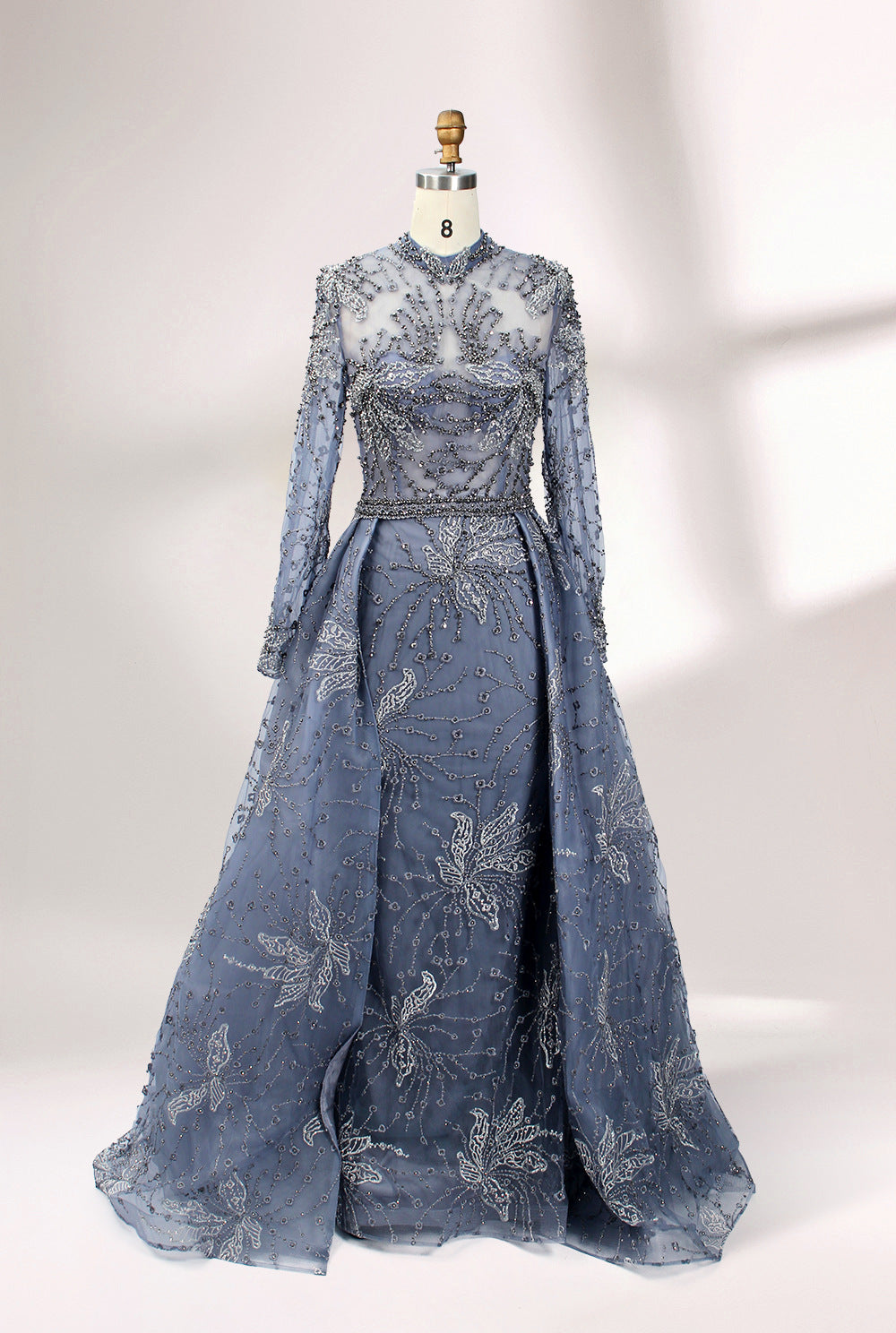 Presented on a mannequin is a blue - toned evening gown. It has a high neckline, long sheer sleeves, and intricate floral embroidery. The elegant design gives off a luxurious and sophisticated vibe, ideal for formal occasions.3