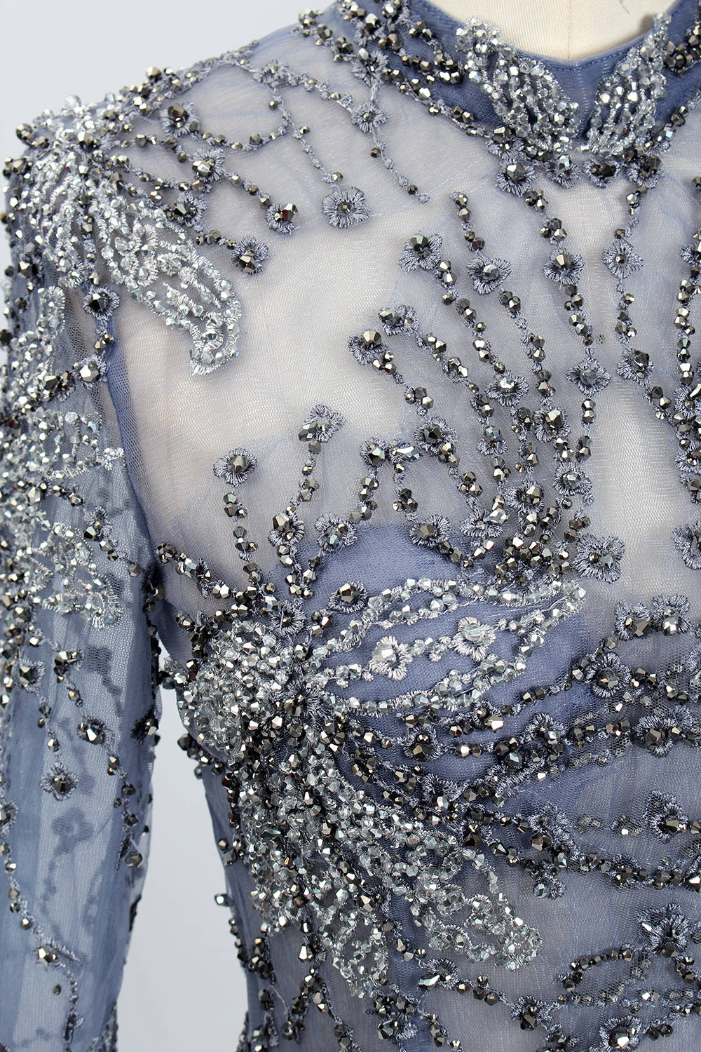 Presented on a mannequin is a blue - toned evening gown. It has a high neckline, long sheer sleeves, and intricate floral embroidery. The elegant design gives off a luxurious and sophisticated vibe, ideal for formal occasions.6