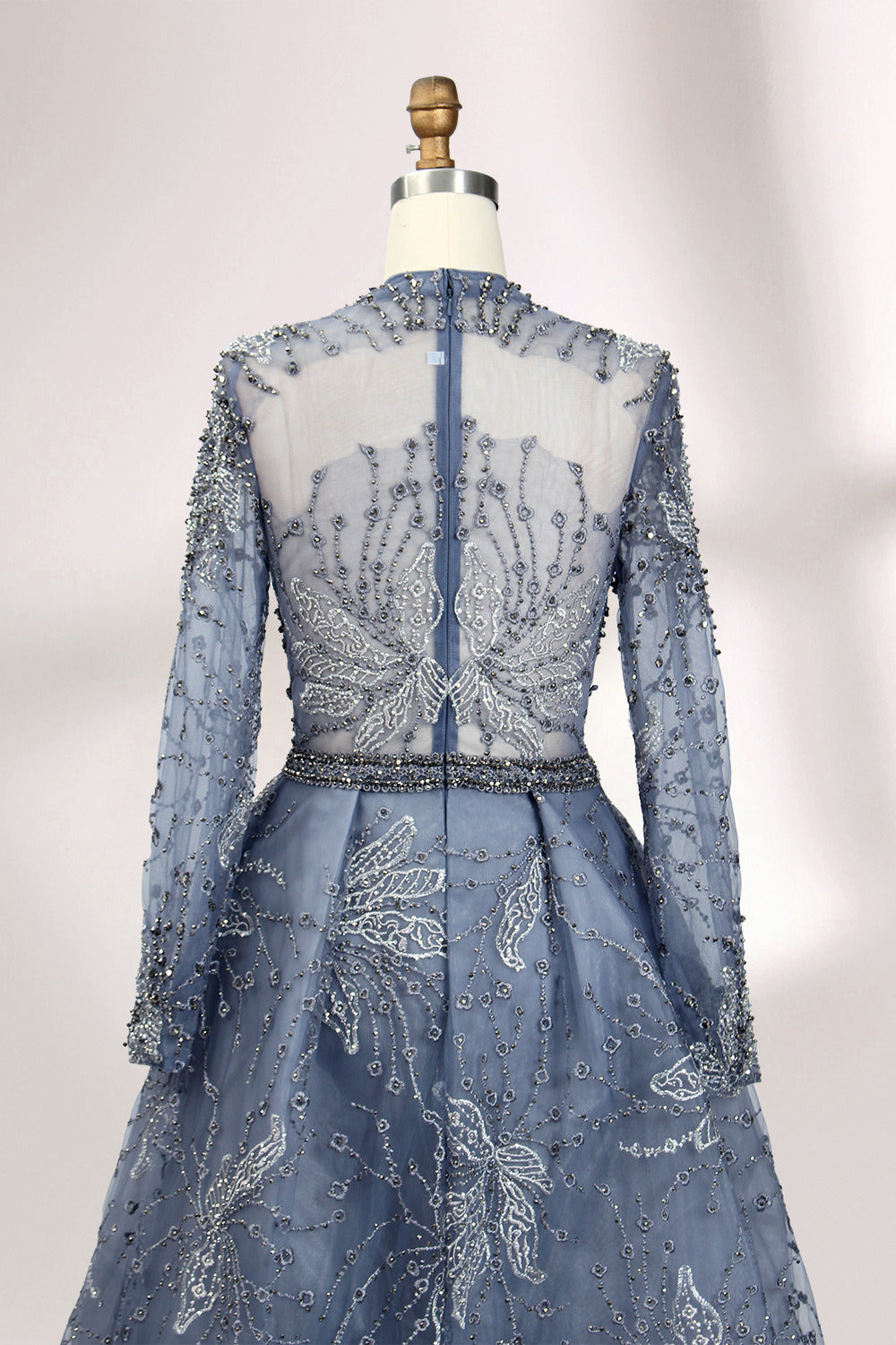 Presented on a mannequin is a blue - toned evening gown. It has a high neckline, long sheer sleeves, and intricate floral embroidery. The elegant design gives off a luxurious and sophisticated vibe, ideal for formal occasions.8