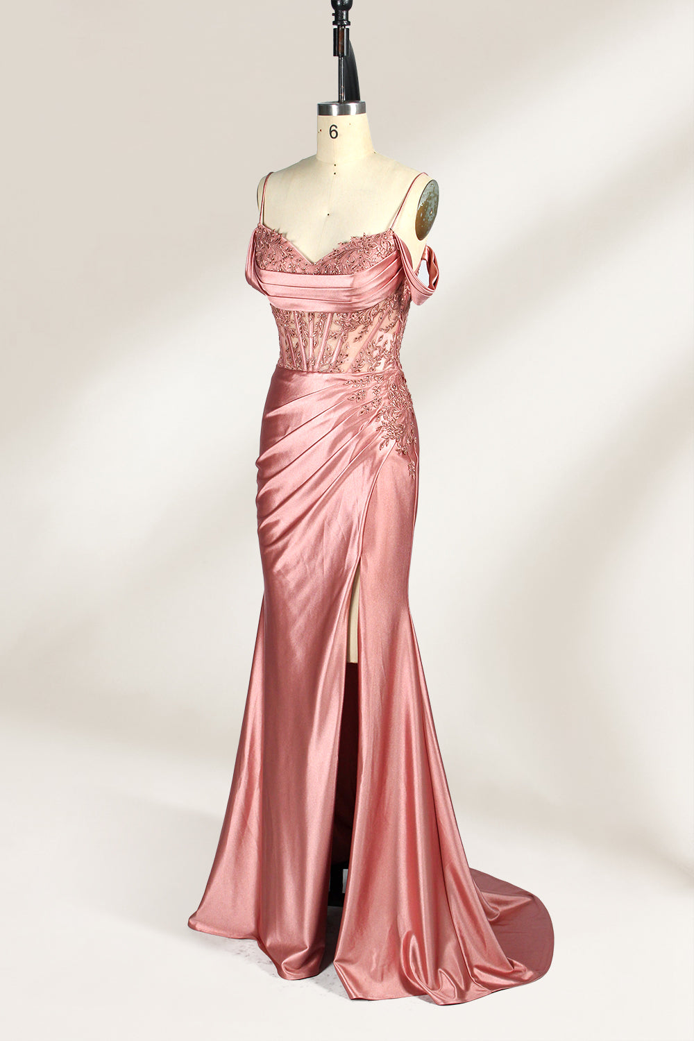 A mannequin displays a rose - gold satin gown. It has thin straps, off - shoulder lace - detailed sleeves, a ruched bodice, and a high side slit. The elegant design, blending satin and lace, suits formal events like galas or weddings.4