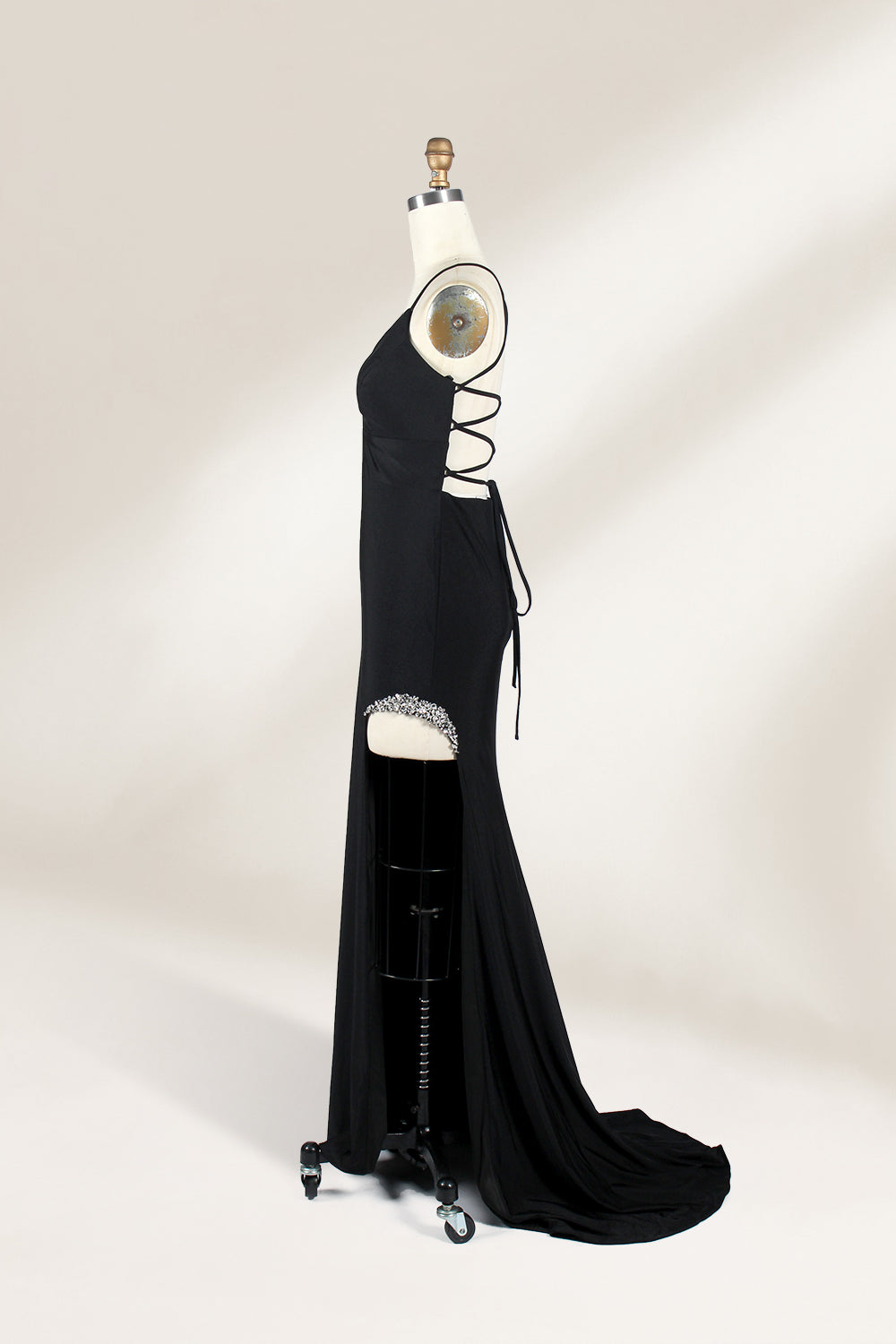 Displayed on a mannequin is a black evening gown. It features spaghetti straps, a deep V - neck, and a high slit with crystal detailing, creating a sleek and glamorous look for formal events.5