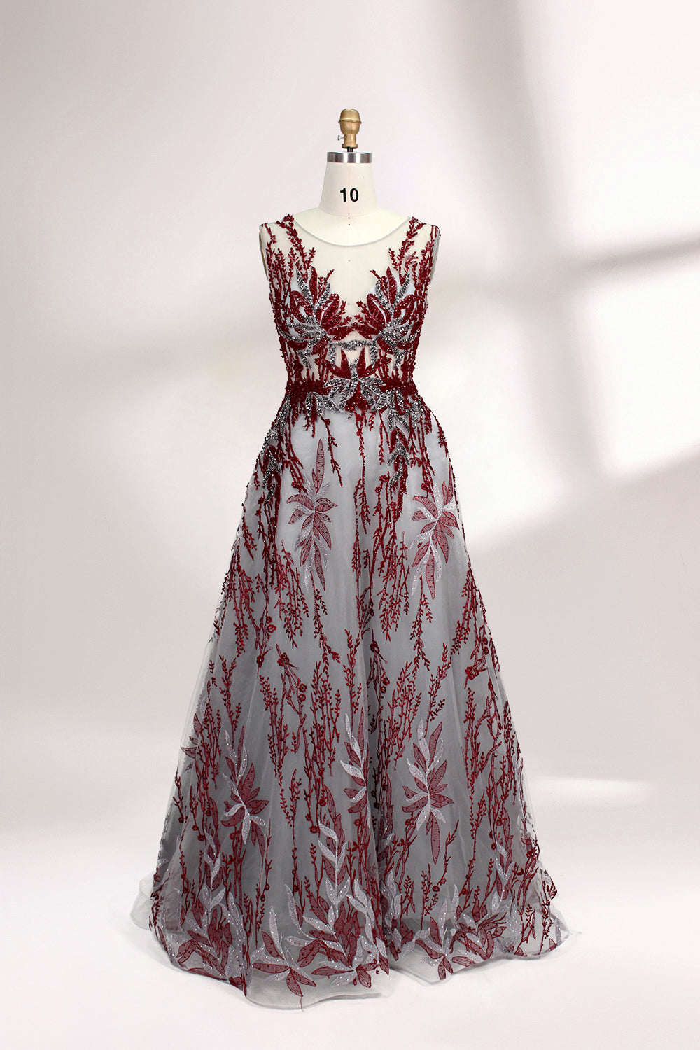 Presented on a mannequin is a gown with a gray base and rich red floral embroidery. It features a sheer neckline, a sleeveless design, and an intricate pattern that gives off a romantic and elegant vibe, perfect for formal events.1