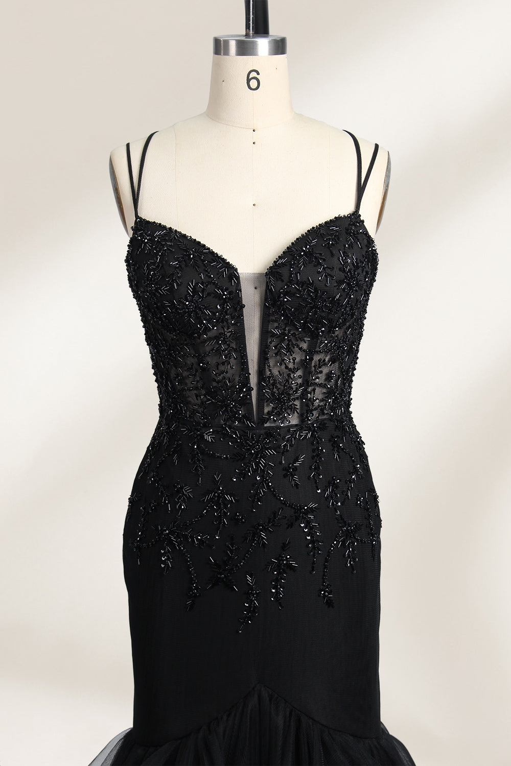 A mannequin displays a black mermaid - style gown. It has thin straps, a deep V - neckline with sheer panels, and intricate black bead embroidery. The layered tulle skirt adds a romantic touch, perfect for formal events like galas or weddings, exuding elegance and sophistication.3