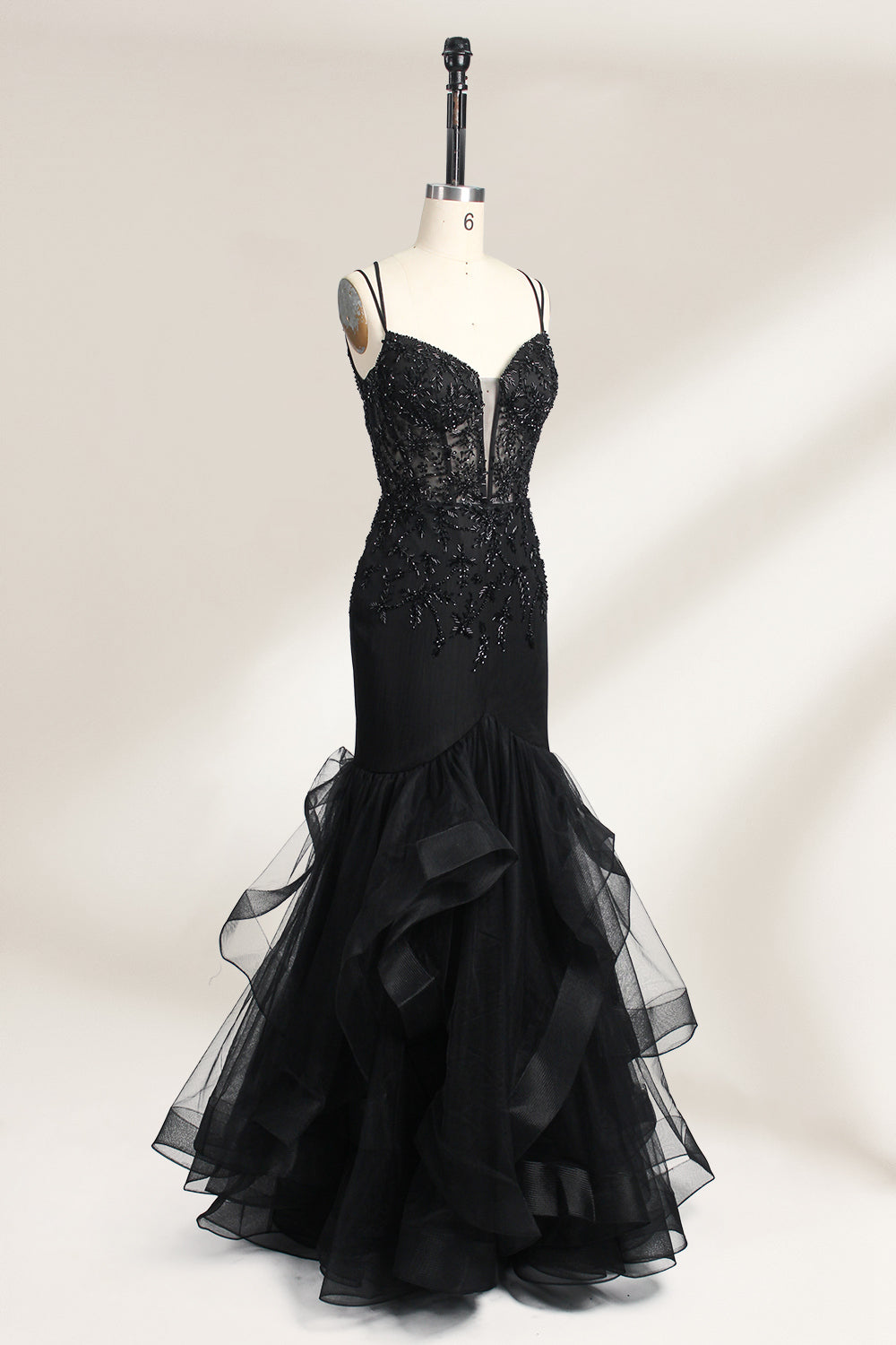 A mannequin displays a black mermaid - style gown. It has thin straps, a deep V - neckline with sheer panels, and intricate black bead embroidery. The layered tulle skirt adds a romantic touch, perfect for formal events like galas or weddings, exuding elegance and sophistication.4