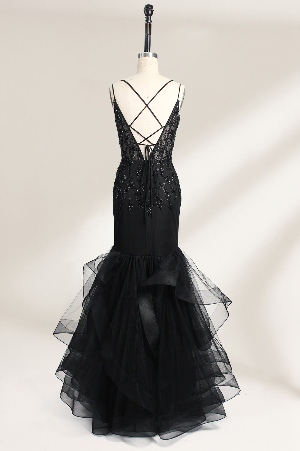 A mannequin displays a black mermaid - style gown. It has thin straps, a deep V - neckline with sheer panels, and intricate black bead embroidery. The layered tulle skirt adds a romantic touch, perfect for formal events like galas or weddings, exuding elegance and sophistication.2