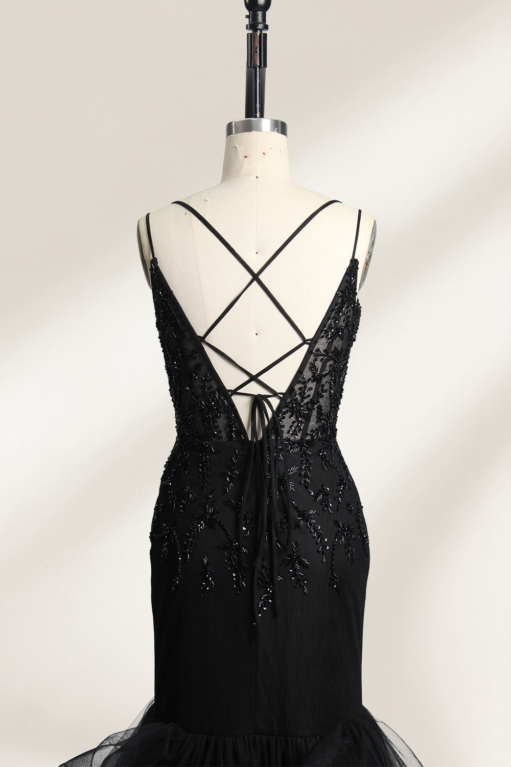 A mannequin displays a black mermaid - style gown. It has thin straps, a deep V - neckline with sheer panels, and intricate black bead embroidery. The layered tulle skirt adds a romantic touch, perfect for formal events like galas or weddings, exuding elegance and sophistication.5