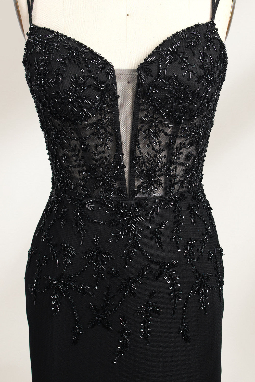 A mannequin displays a black mermaid - style gown. It has thin straps, a deep V - neckline with sheer panels, and intricate black bead embroidery. The layered tulle skirt adds a romantic touch, perfect for formal events like galas or weddings, exuding elegance and sophistication.6