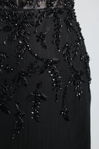 A mannequin displays a black mermaid - style gown. It has thin straps, a deep V - neckline with sheer panels, and intricate black bead embroidery. The layered tulle skirt adds a romantic touch, perfect for formal events like galas or weddings, exuding elegance and sophistication.7